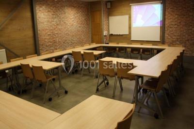 Salle de conférence vide avec des rangées de chaises en bois, un écran de projection et des tableaux accrochés au mur.