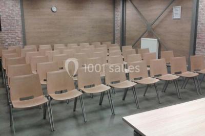 Salle de conférence vide avec des rangées de chaises en bois, un écran de projection et des tableaux accrochés au mur.