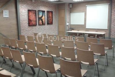 Salle de conférence vide avec des rangées de chaises en bois, un écran de projection et des tableaux accrochés au mur.
