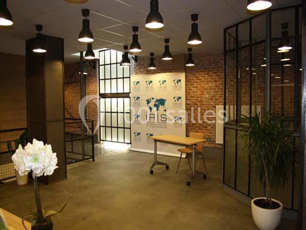 Espace de bureau moderne avec murs en briques, plantes, éclairage suspendu et panneau affichant le logo ’IRIS’.