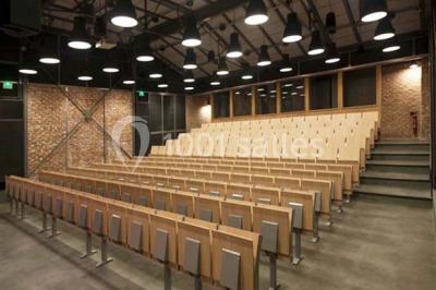 Salle de conférence vide avec des rangées de chaises en bois, un écran de projection et des tableaux accrochés au mur.