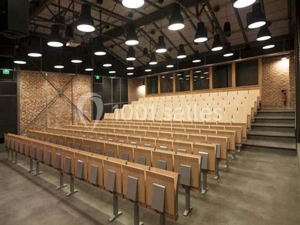 Salle de conférence moderne avec des rangées de sièges en bois et un mur en briques apparentes.