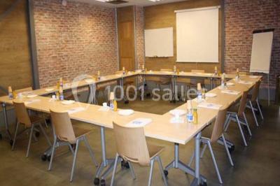 Salle de conférence vide avec des rangées de chaises en bois, un écran de projection et des tableaux accrochés au mur.