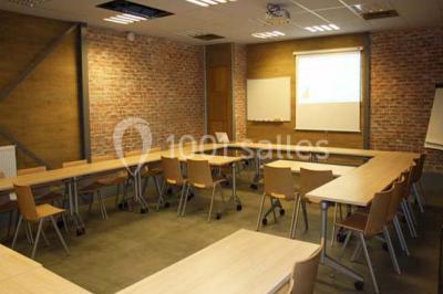 Salle de conférence vide avec des rangées de chaises en bois, un écran de projection et des tableaux accrochés au mur.