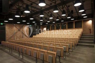 Salle de conférence vide avec des rangées de chaises en bois, un écran de projection et des tableaux accrochés au mur.