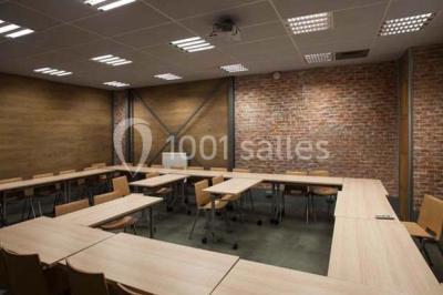 Salle de conférence vide avec des rangées de chaises en bois, un écran de projection et des tableaux accrochés au mur.