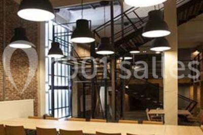 Salle de conférence vide avec des rangées de chaises en bois, un écran de projection et des tableaux accrochés au mur.