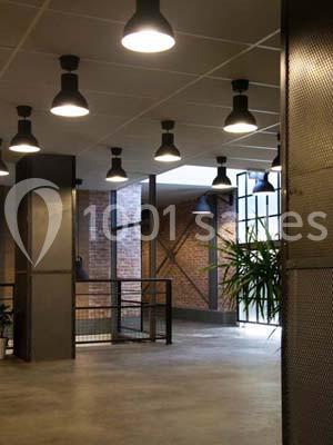 Espace intérieur industriel avec murs en briques, grandes fenêtres, luminaires suspendus et plantes décoratives.