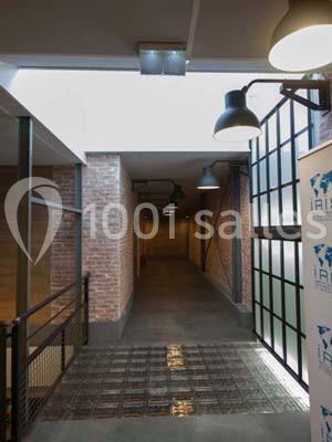 Couloir industriel avec murs en briques, sol en béton, verrière et éclairage suspendu.