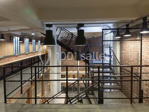 Vue intérieure d'un bâtiment industriel rénové avec des escaliers métalliques, des murs en briques et des luminaires…