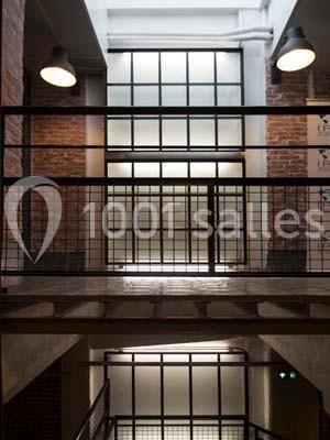 Escalier intérieur industriel avec murs en briques, garde-corps métalliques et grandes fenêtres vitrées.