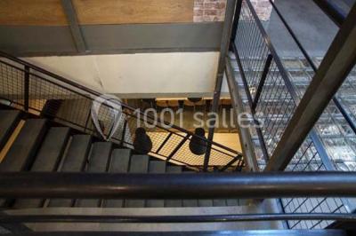 Salle de conférence vide avec des rangées de chaises en bois, un écran de projection et des tableaux accrochés au mur.