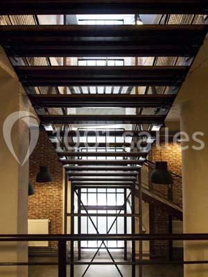 Escalier métallique suspendu dans un intérieur industriel avec murs en briques et grandes fenêtres.