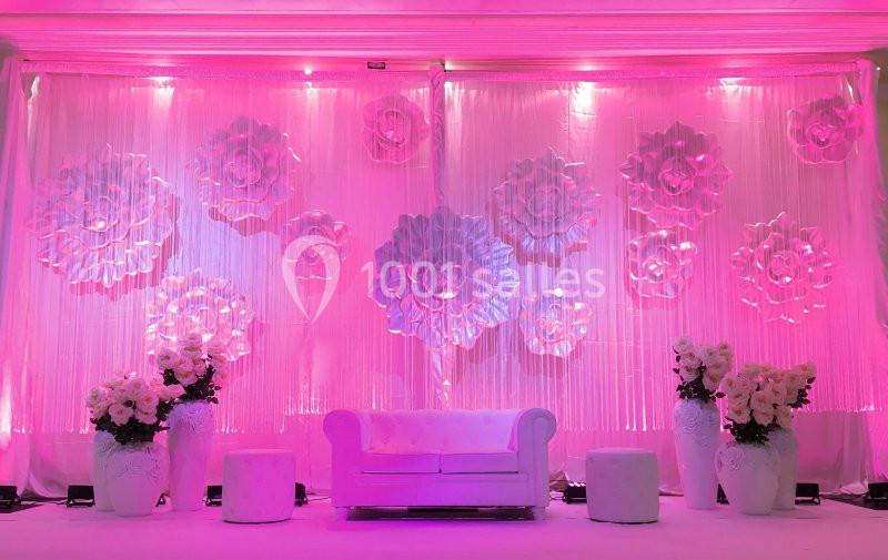 Décor intérieur avec un canapé blanc, des fleurs en relief sur un rideau rose illuminé et des vases de fleurs blanches.