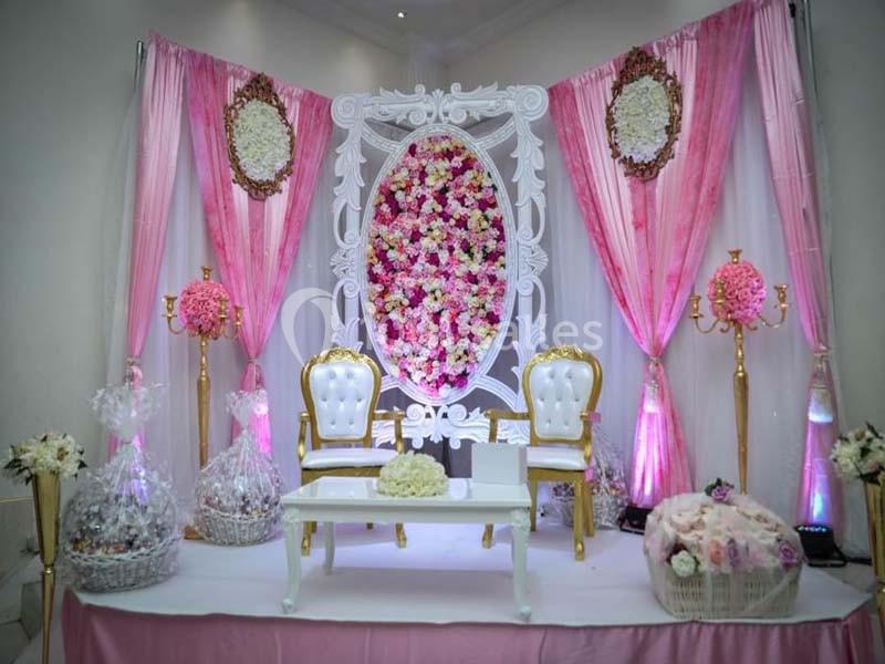 Décor de mariage avec fauteuils dorés, table blanche, rideaux roses et arrangements floraux en arrière-plan.