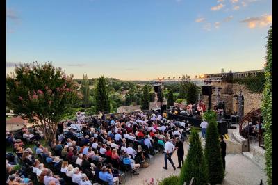 Un concert en plein air au coucher du soleil, avec un public assis devant une scène entourée de verdure.