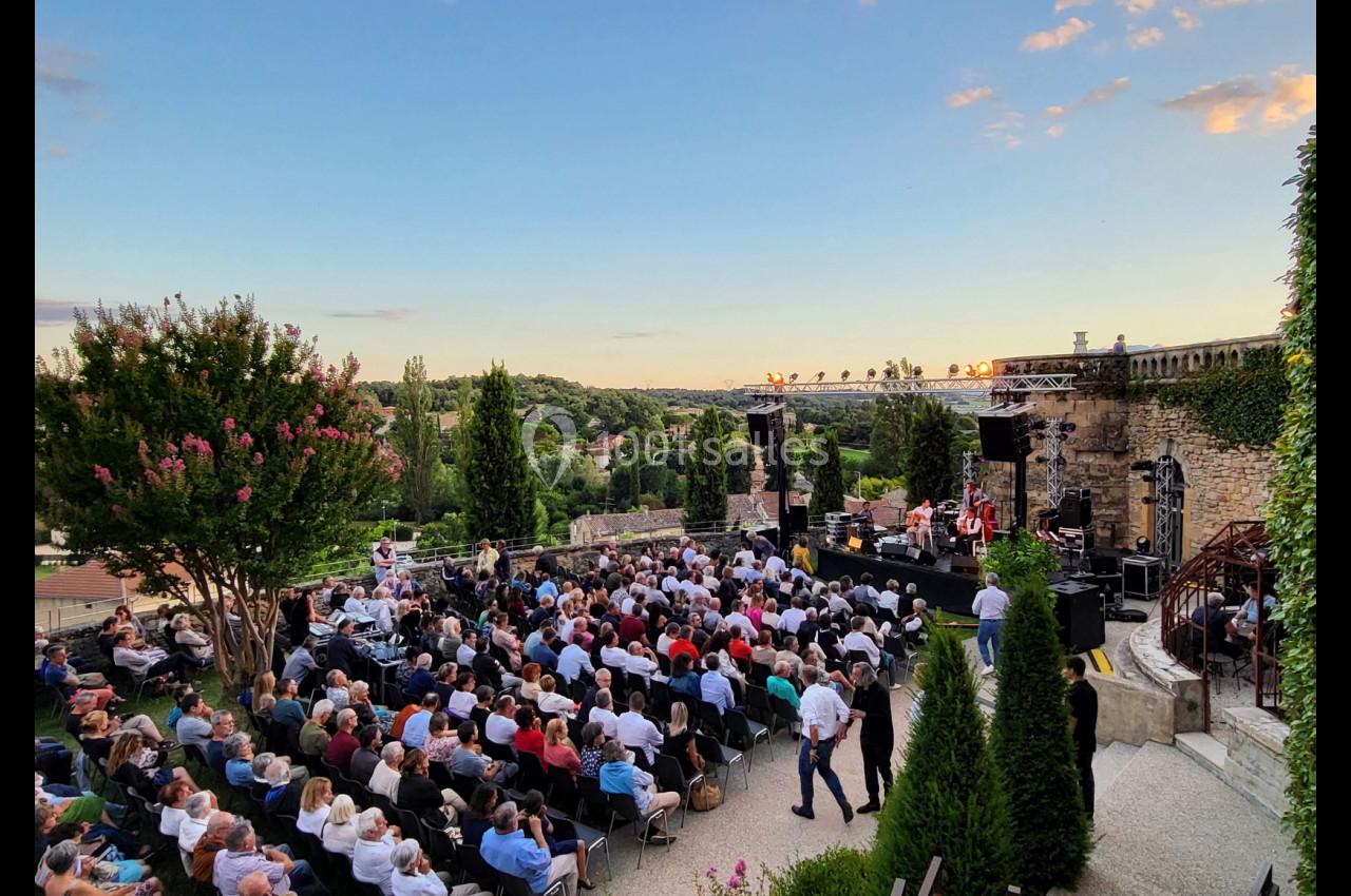 Un concert en plein air au coucher du soleil, avec un public assis devant une scène entourée de verdure.