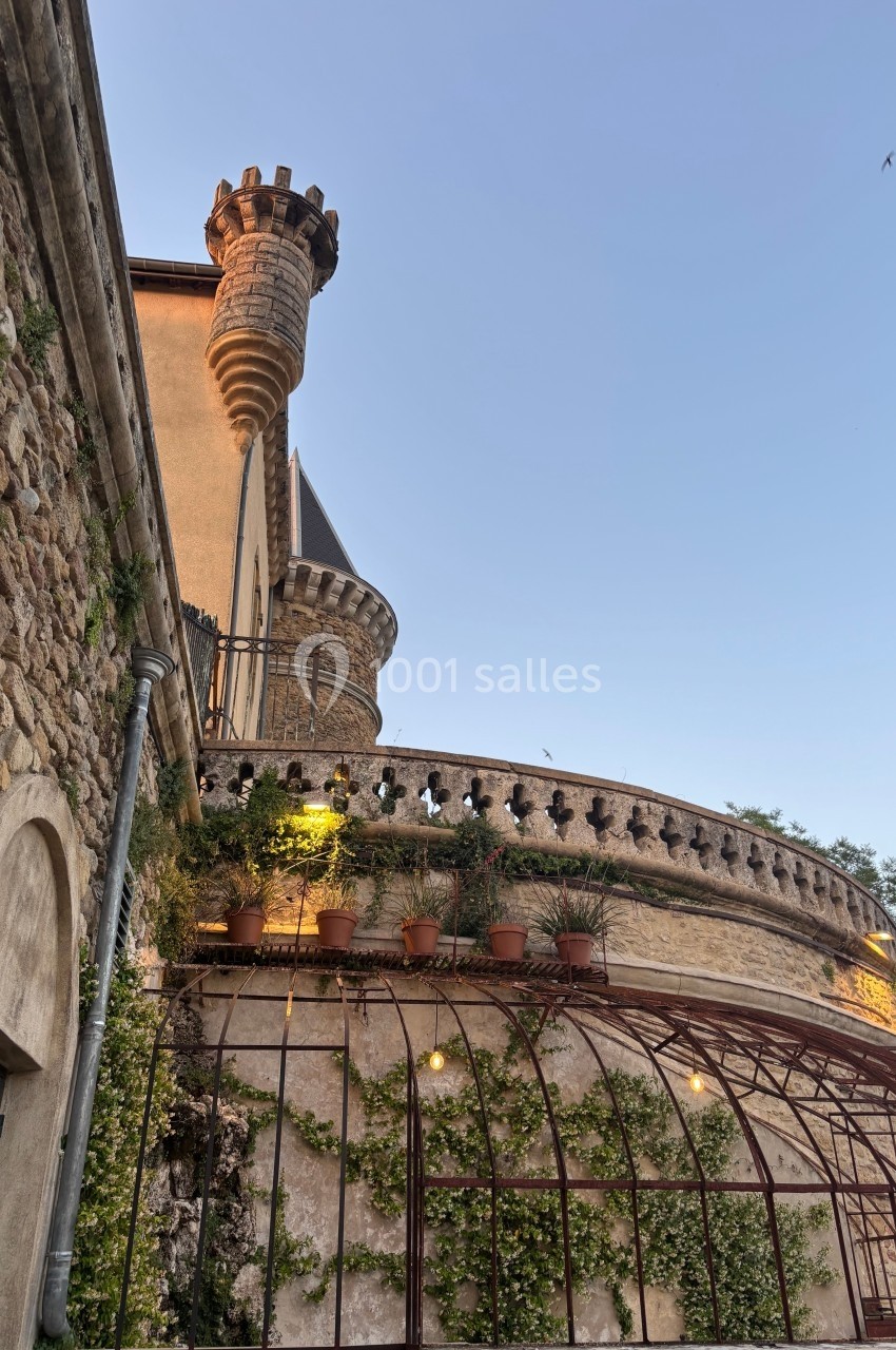 Façade en pierre d'un bâtiment ancien avec une tour, des plantes grimpantes et un ciel dégagé en arrière-plan.