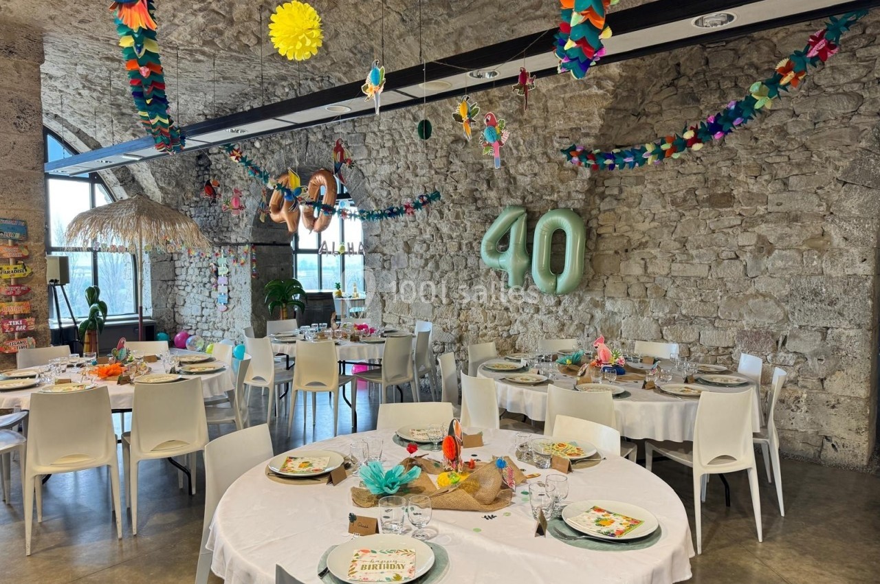 Salle décorée pour une fête d'anniversaire avec des tables rondes dressées, des guirlandes colorées et un ballon ’40’.