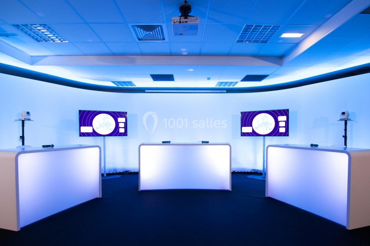 Plateau de présentation moderne avec trois pupitres éclairés, deux écrans et un éclairage bleu ambiant.