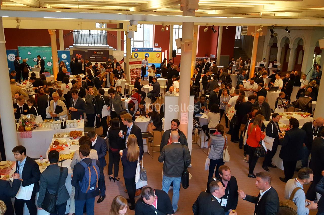Salle animée avec de nombreux participants échangeant autour de stands lors d'un événement professionnel.