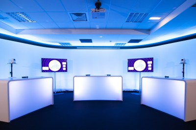 Salle de conférence vide avec rangées de sièges rouges, écran de projection et éclairage fluorescent.