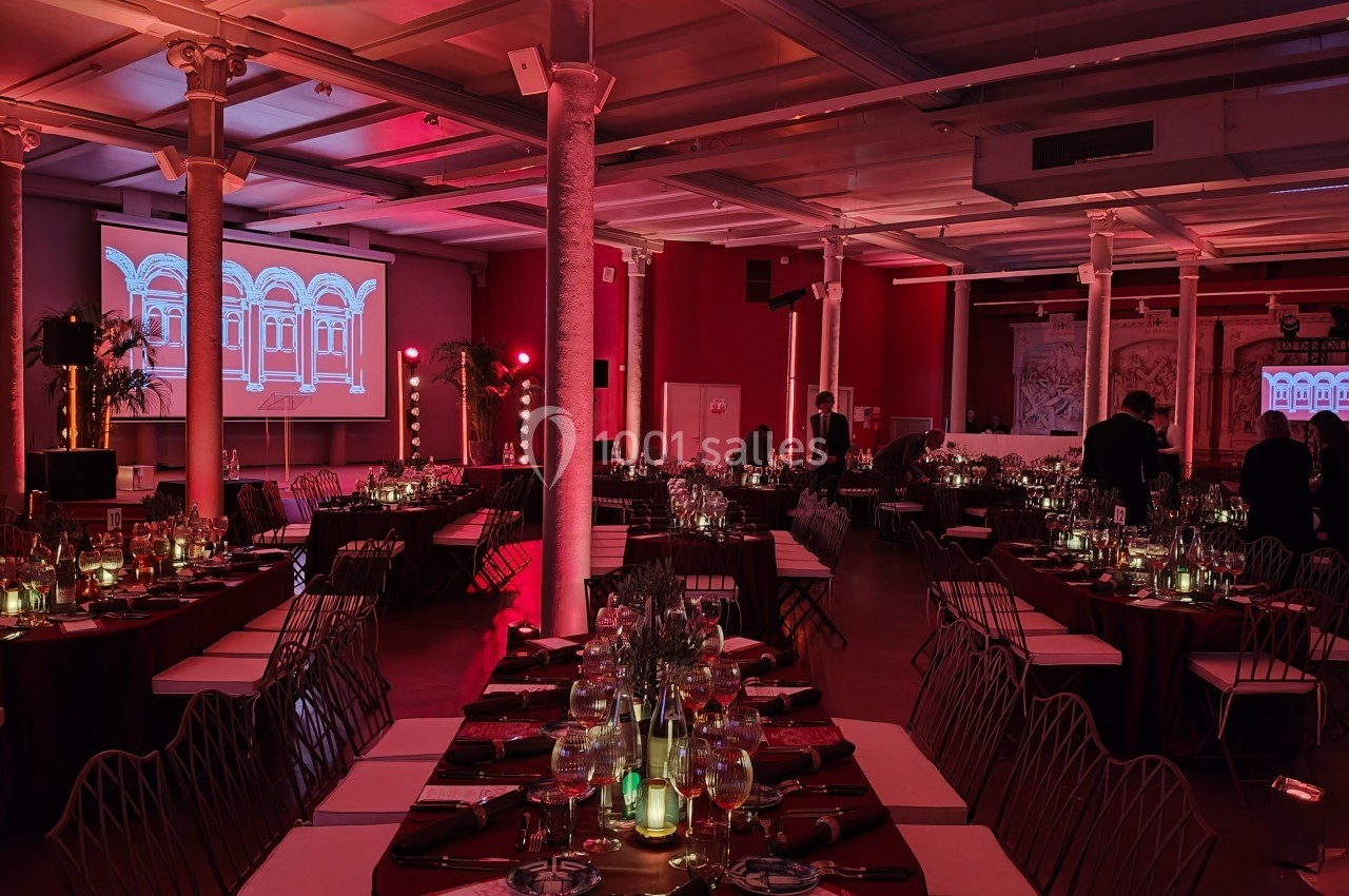 Salle de réception décorée avec des tables dressées, éclairage rouge tamisé et écrans projetant des images architecturales.