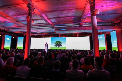 Salle de conférence vide avec rangées de sièges rouges, écran de projection et éclairage fluorescent.