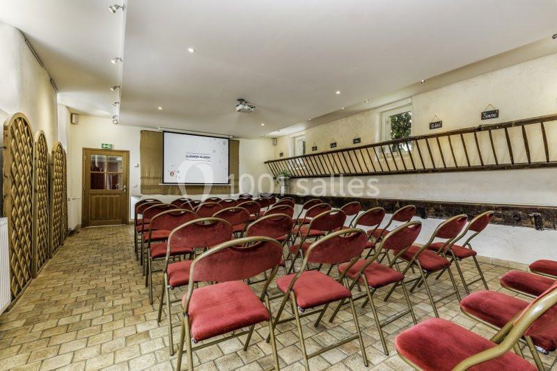 Salle de réunion avec des chaises rouges alignées, un écran de projection et des murs décorés de bois et d'échelles.