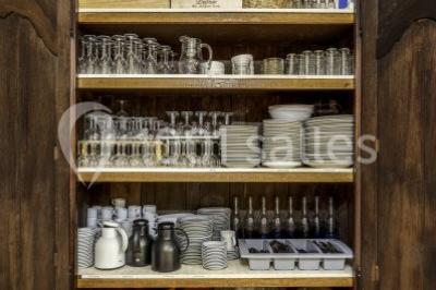 Armoire en bois ouverte contenant des verres, assiettes, bols, carafes et paniers soigneusement rangés sur des étagères.