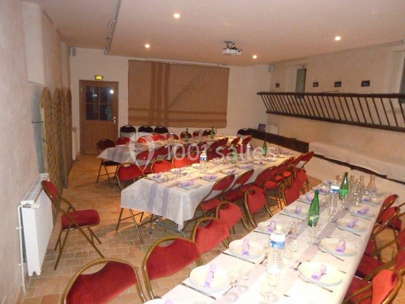 Salle de réception avec tables dressées, nappes blanches et chaises rouges, prête pour un repas ou un événement.