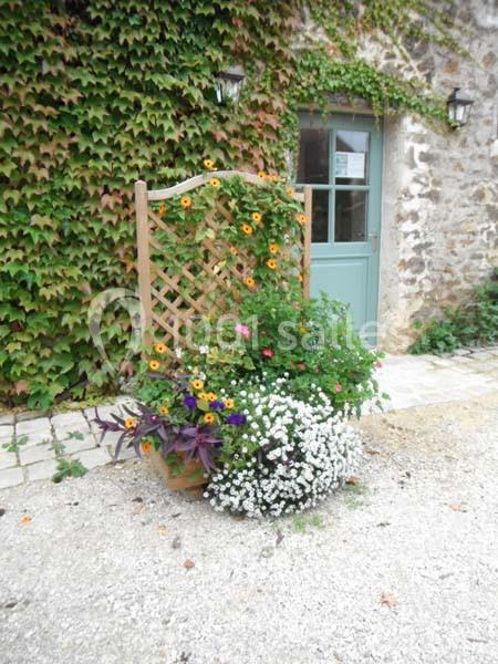Treillis en bois décoré de fleurs colorées devant un mur en pierre recouvert de lierre et une porte verte.