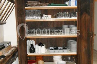 Armoire en bois ouverte contenant des verres, assiettes, bols et carafes, organisée sur plusieurs étagères.