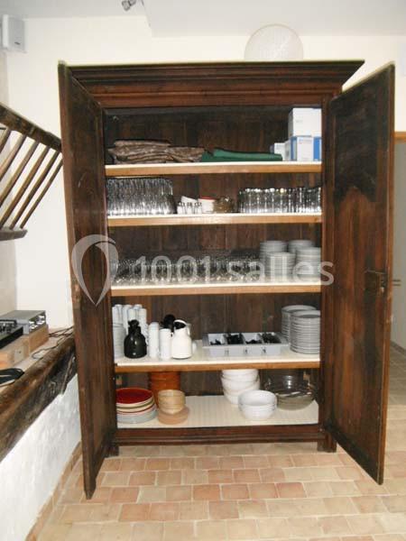 Armoire en bois ouverte contenant des verres, assiettes, bols et carafes, organisée sur plusieurs étagères.
