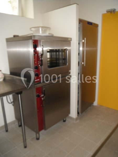 Four professionnel en acier inoxydable avec commandes visibles, placé dans une cuisine équipée d'un réfrigérateur.