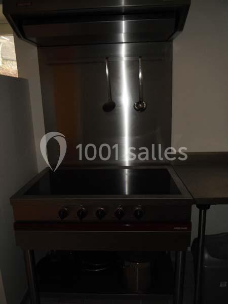 Plaque de cuisson vitrocéramique avec hotte en inox et ustensiles suspendus dans une cuisine sobre.