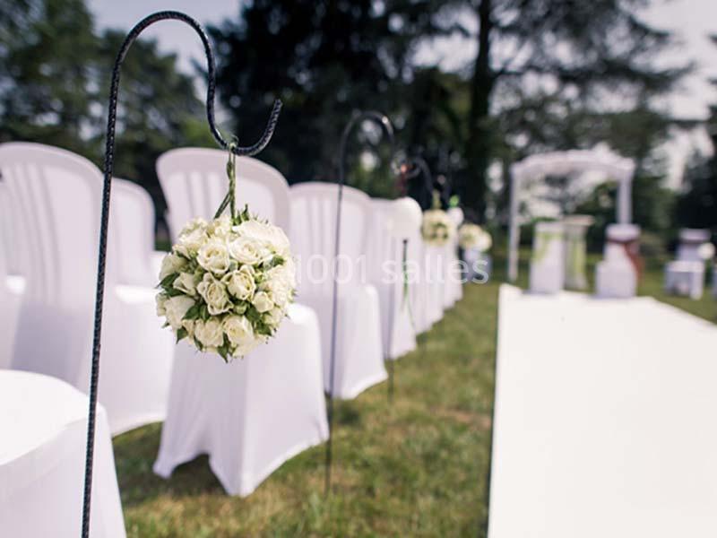 Allée décorée de chaises blanches et de bouquets de fleurs pour une cérémonie en extérieur.