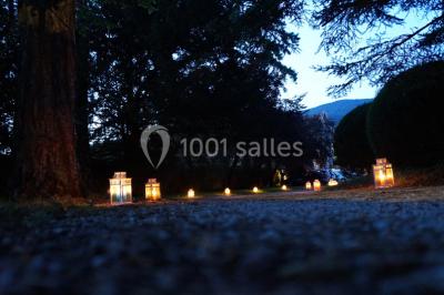 Un jardin verdoyant avec pelouse, arbustes et grands arbres, devant une tour en pierre sous un ciel légèrement nuageux.