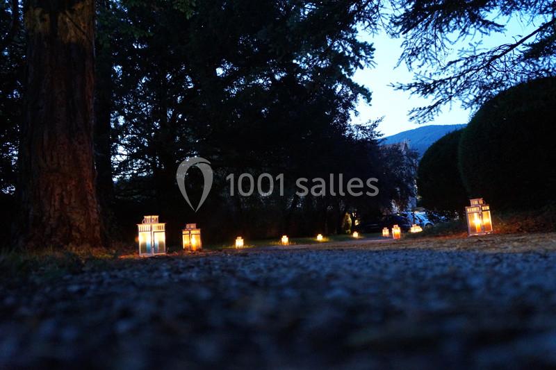 Chemin bordé de lanternes allumées au crépuscule, entouré d'arbres et de végétation.