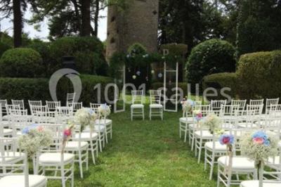 Un jardin verdoyant avec pelouse, arbustes et grands arbres, devant une tour en pierre sous un ciel légèrement nuageux.