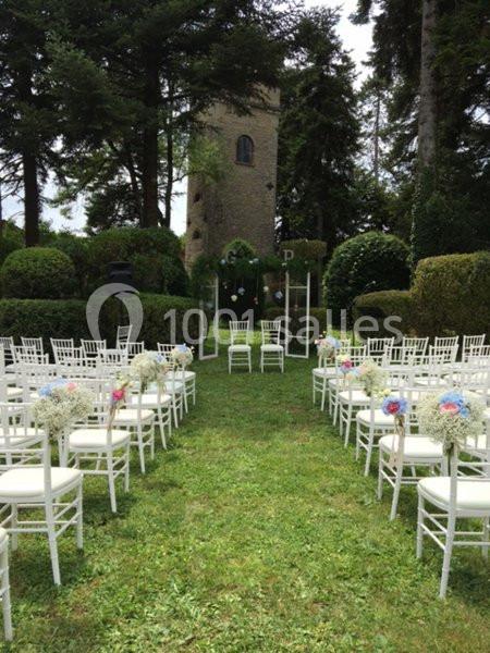Chaises blanches alignées en extérieur, décorées de fleurs, avec une tour en pierre en arrière-plan.