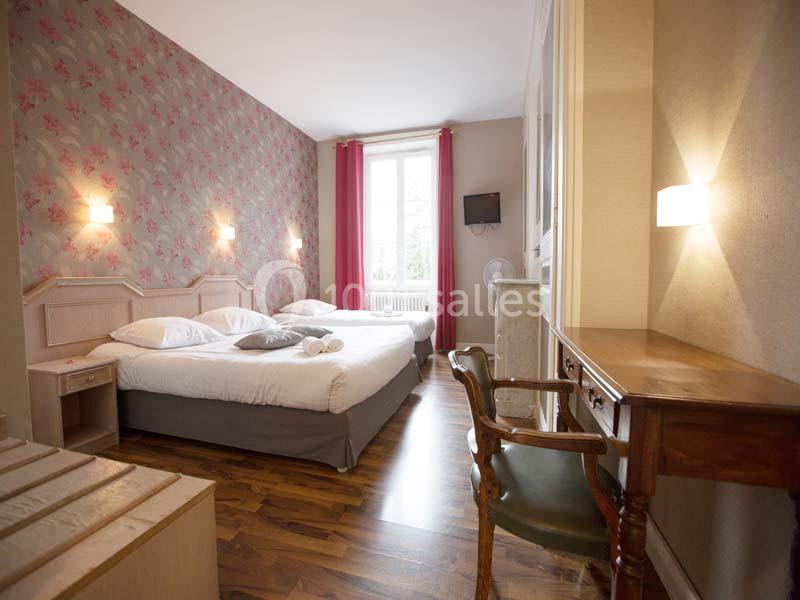 Chambre lumineuse avec un lit double, un bureau en bois, des murs décorés de papier peint fleuri et un sol en parquet.