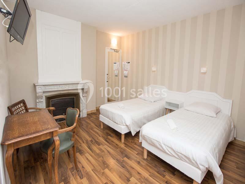 Chambre avec deux lits simples, un bureau en bois, une cheminée décorative et un sol en parquet.