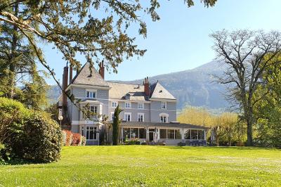 Un jardin verdoyant avec pelouse, arbustes et grands arbres, devant une tour en pierre sous un ciel légèrement nuageux.