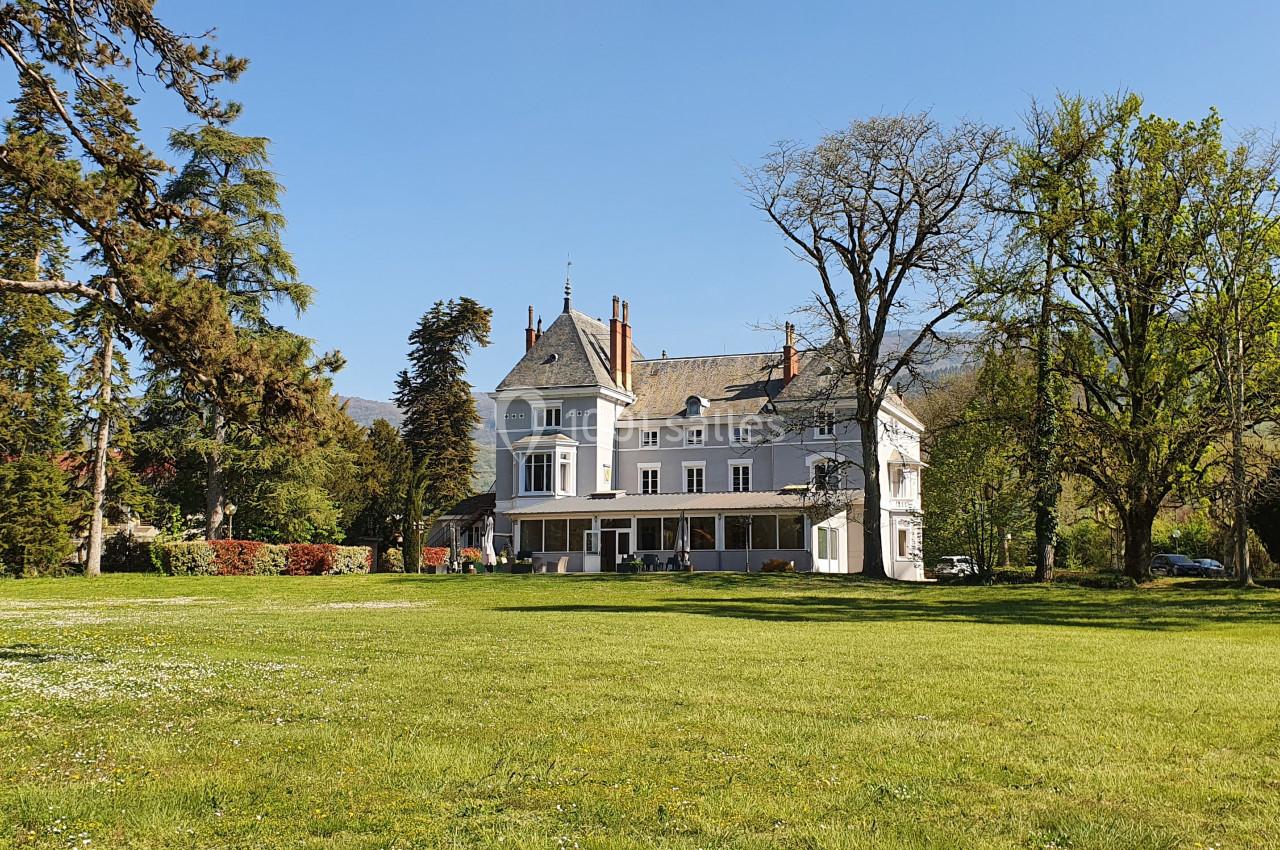 Grande maison de style classique entourée d'arbres et d'une pelouse verdoyante sous un ciel dégagé.