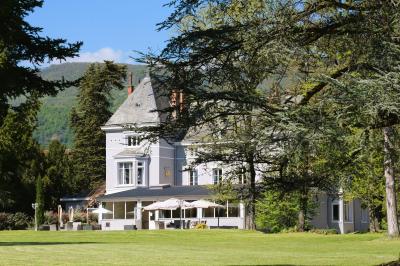 Un jardin verdoyant avec pelouse, arbustes et grands arbres, devant une tour en pierre sous un ciel légèrement nuageux.