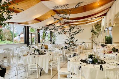 Un jardin verdoyant avec pelouse, arbustes et grands arbres, devant une tour en pierre sous un ciel légèrement nuageux.
