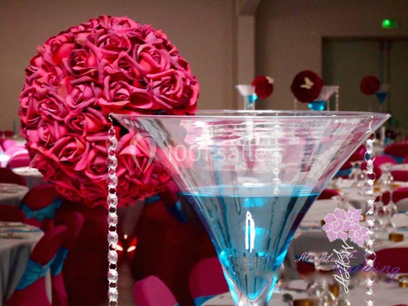 Centre de table avec une boule de roses rouges suspendue et un grand verre rempli de liquide bleu.