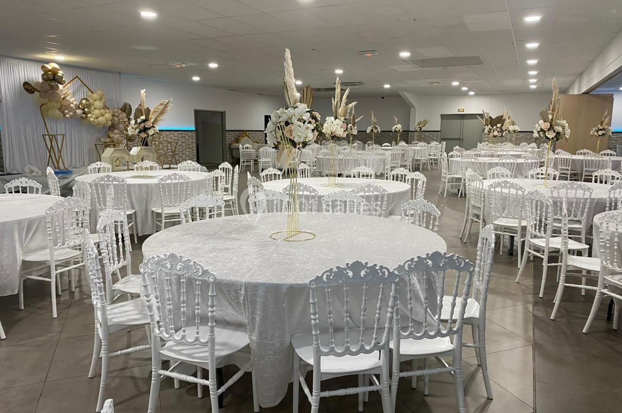 Salle de réception décorée avec des tables rondes drapées de nappes blanches et des chaises assorties, ornée de fleurs et…