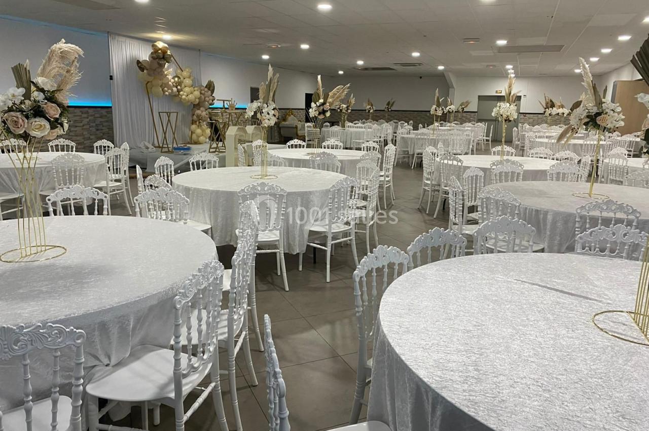 Salle de réception décorée avec des tables rondes recouvertes de nappes blanches et des compositions florales élégantes.